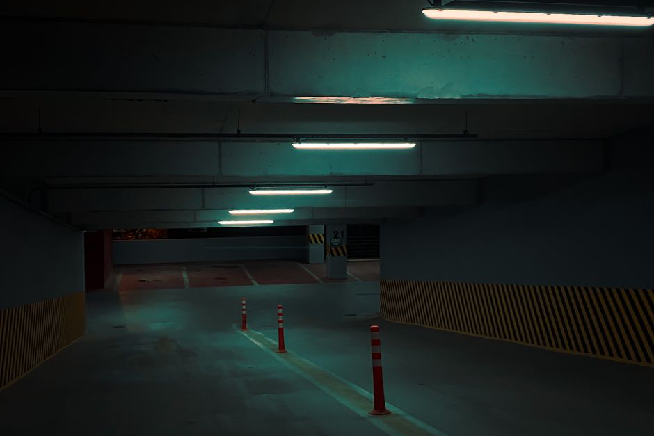 Moody view of a dimly lit underground parking garage with fluorescent lights and orange bollards.